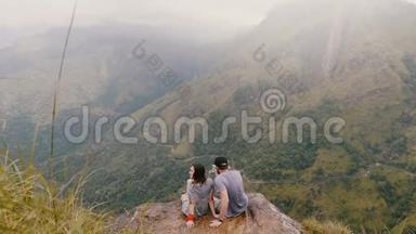 在斯里兰卡史诗般的山景中，仰视高角度、快乐、浪漫的新婚夫妇在雨中坐在一起。